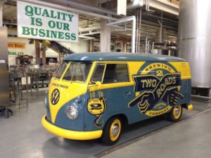 A yellow and blue vw bus is parked in a factory.